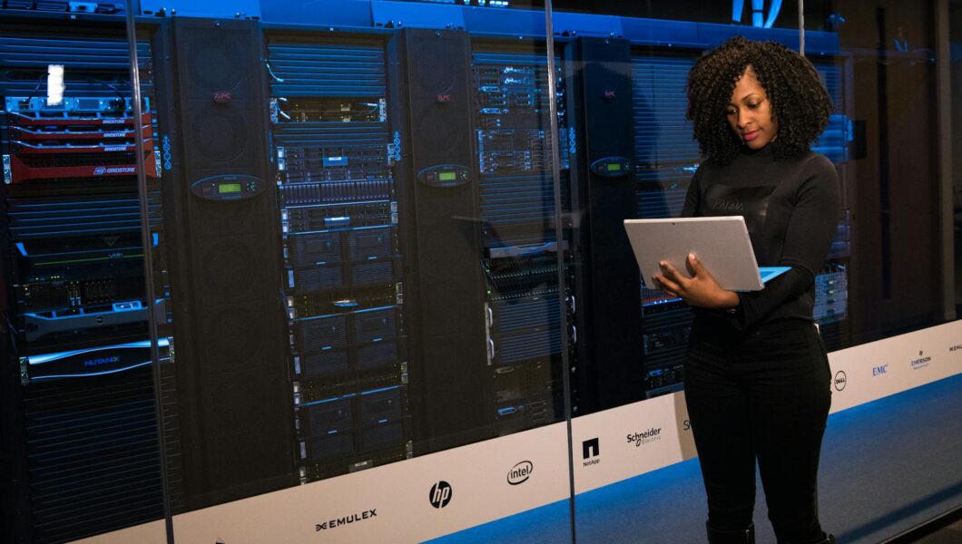 A female engineer using a laptop while monitoring data servers in a modern server room.