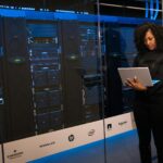 A female engineer using a laptop while monitoring data servers in a modern server room.